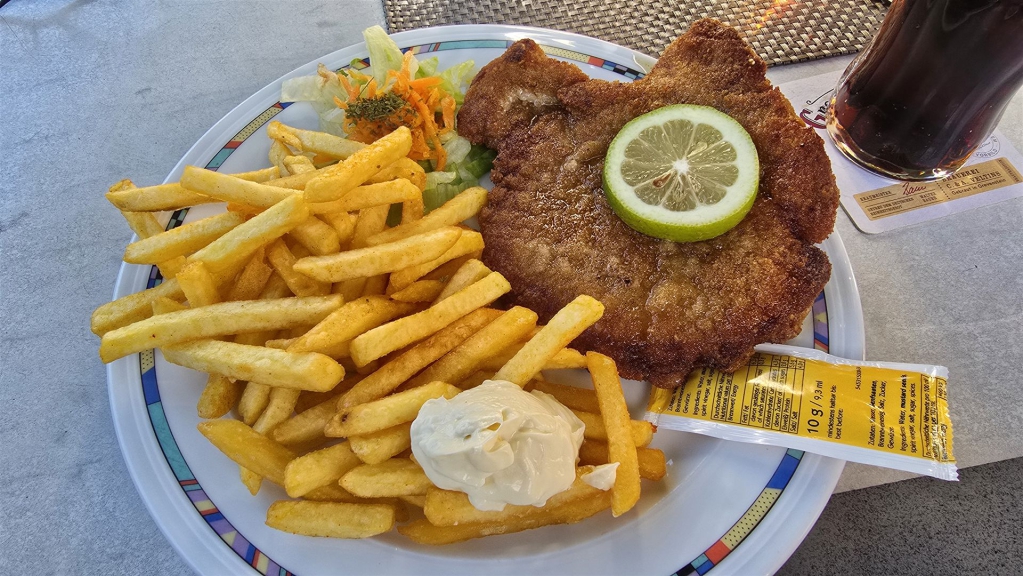 Ein Teller mit paniertem Hauptgericht, Pommes frites, Dip-Sauce und Zitronenscheibe.